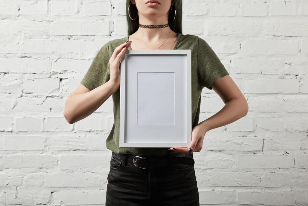 обрізаний вид жінки, що стоїть і тримає порожню білу рамку в руках
 - Фото, зображення
