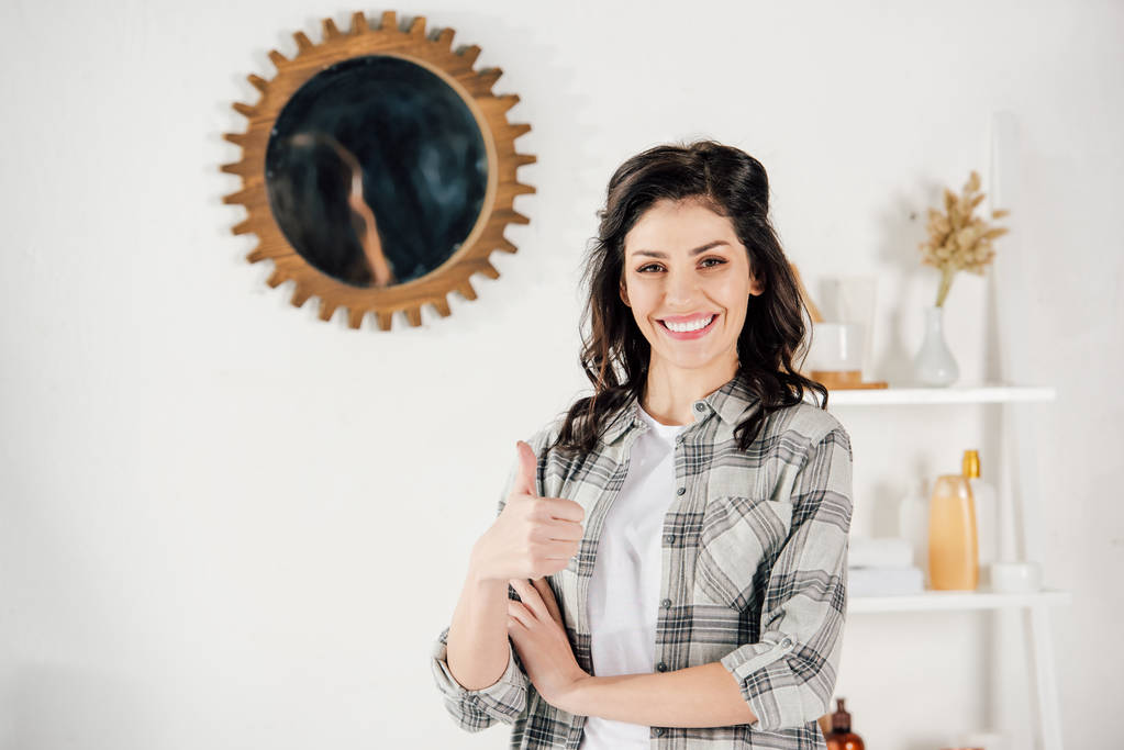 mujer en camisa gris mostrando el pulgar hacia arriba y sonriendo en casa
 - Foto, Imagen