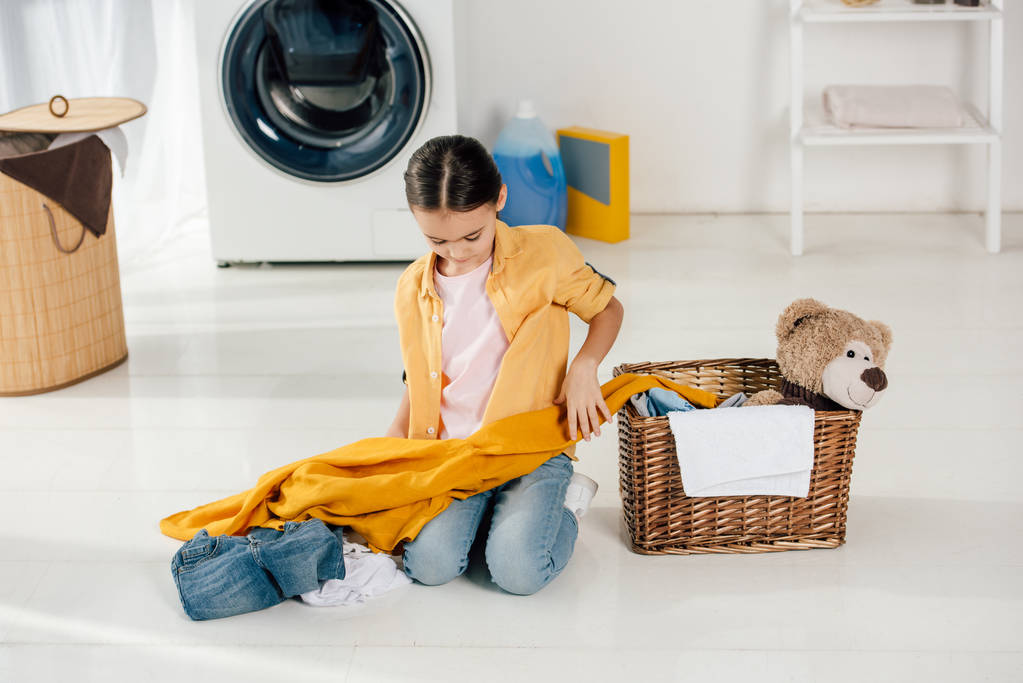 dětské žluté tričko a džíny sedí poblíž koše a oblečení v prádelně - Fotografie, Obrázek