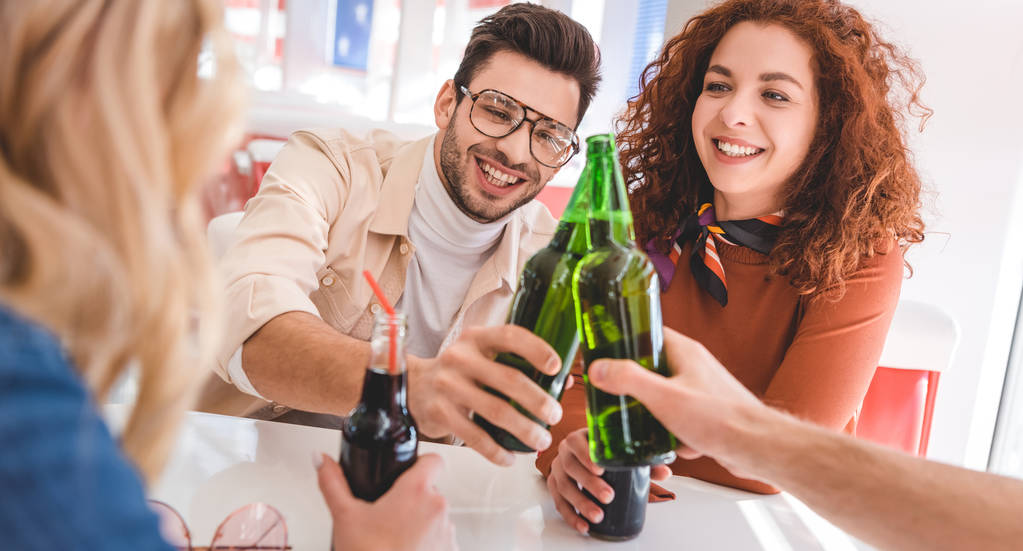 selectieve aandacht van knappe en aantrekkelijke vrienden juichen met glazen flessen en glimlachen  - Foto, afbeelding
