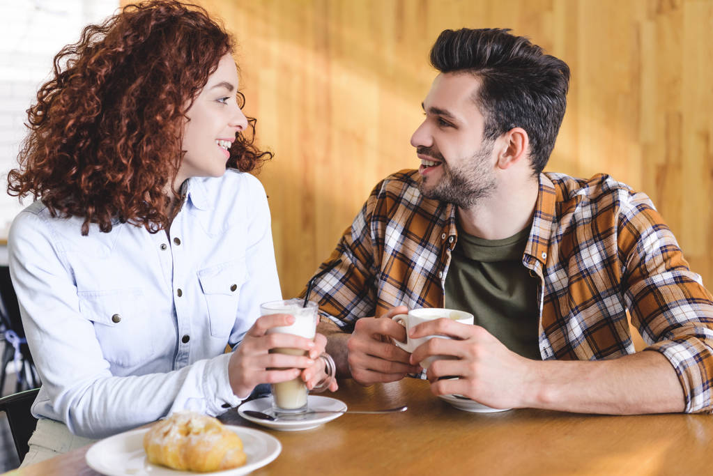 beautiful and smiling couple drinking coffee and looking at each other  - Photo, Image