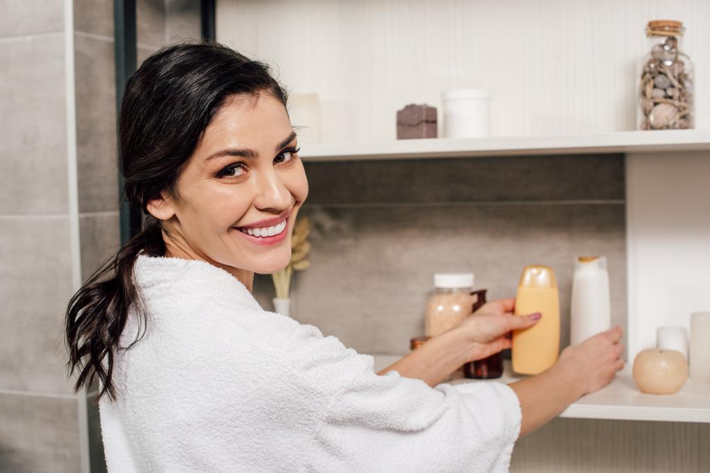 femme prenant des bouteilles avec gel douche des étagères dans la salle de bain
 - Photo, image