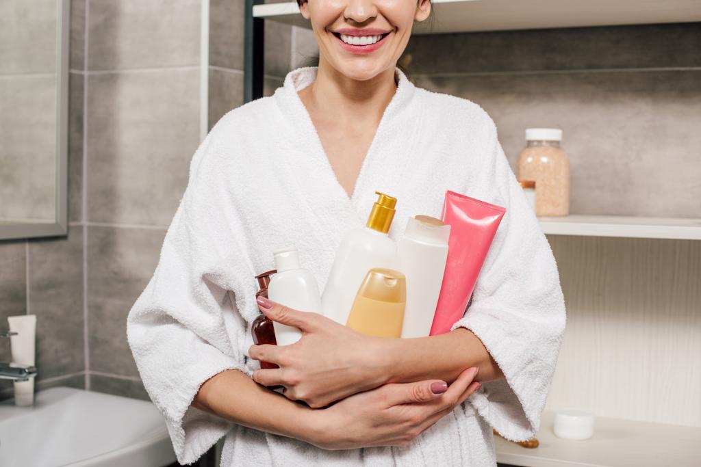 bijgesneden beeld van de vrouw in witte badjas houden van flessen in badkamer - Foto, afbeelding