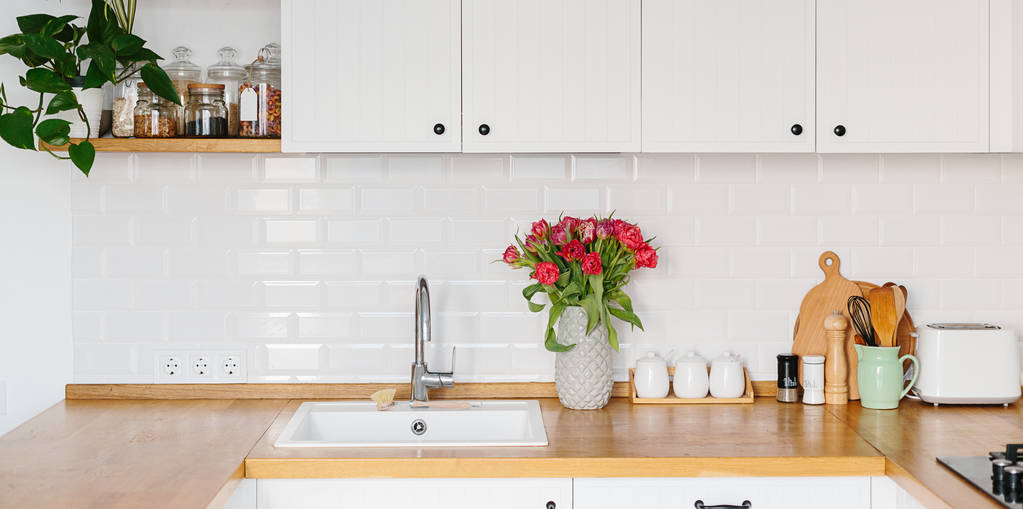 Buquê de tulipas em vaso em pé na bancada de madeira na cozinha. Cozinha moderna em forma de u branco em estilo escandinavo
. - Foto, Imagem