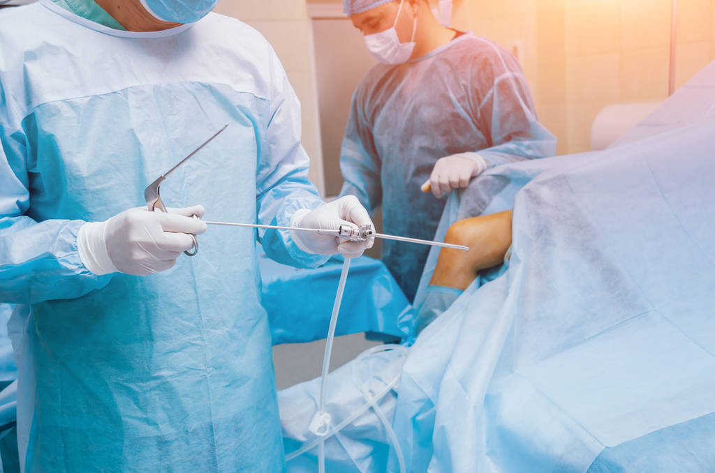 Artroscoop operatie. Orthopedische chirurgen in teamwork in de operatiekamer met moderne artroscopische hulpmiddelen. Knieoperatie. Ziekenhuisachtergrond - Foto, afbeelding
