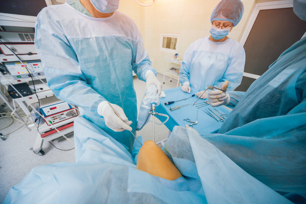 Cirurgia artroscópica. Cirurgiões ortopédicos em equipe na sala de cirurgia com ferramentas artroscópicas modernas. Cirurgia do joelho. Contexto hospitalar
 - Foto, Imagem