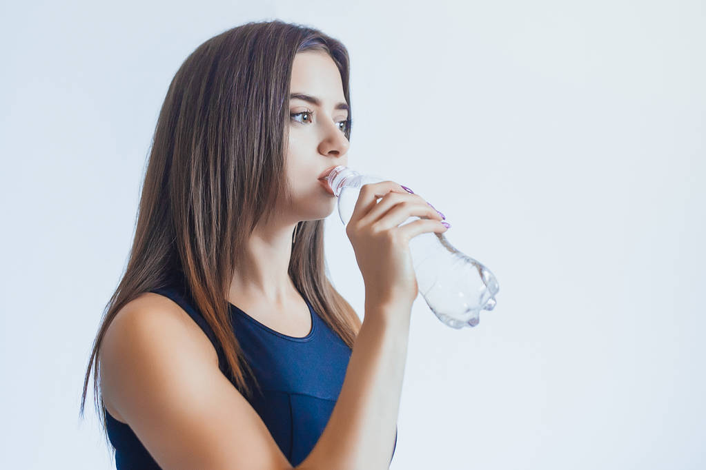 вид збоку молодої жінки, що п'є воду з пляшки
  - Фото, зображення