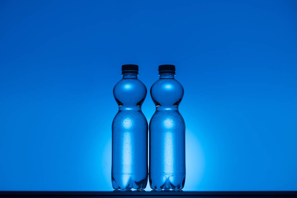 tonda şeffaf plastik su şişeleri üzerinde kopya alanı ve arkadan aydınlatmalı neon mavi arka plan görüntüsünü - Fotoğraf, Görsel