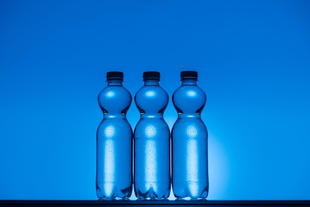 バックライト付きネオン青い背景に透明なプラスチックの水ボトルのトーンのイメージ - 写真・画像