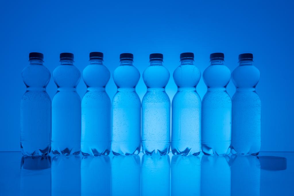 imagen tonificada de botellas de agua de plástico en fila sobre fondo azul neón con retroiluminación
 - Foto, imagen