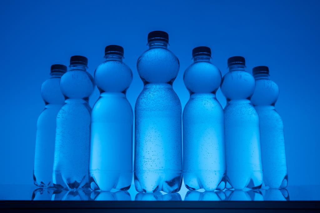 getöntes Bild von Plastikflaschen mit Wasser in Reihe auf neonblauem Hintergrund - Foto, Bild