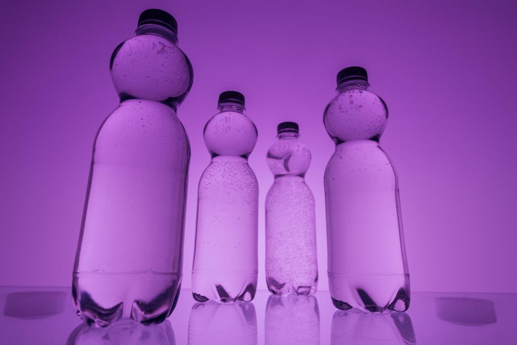 тоноване зображення пластикових пляшок води на неоновому фіолетовому фоні
 - Фото, зображення