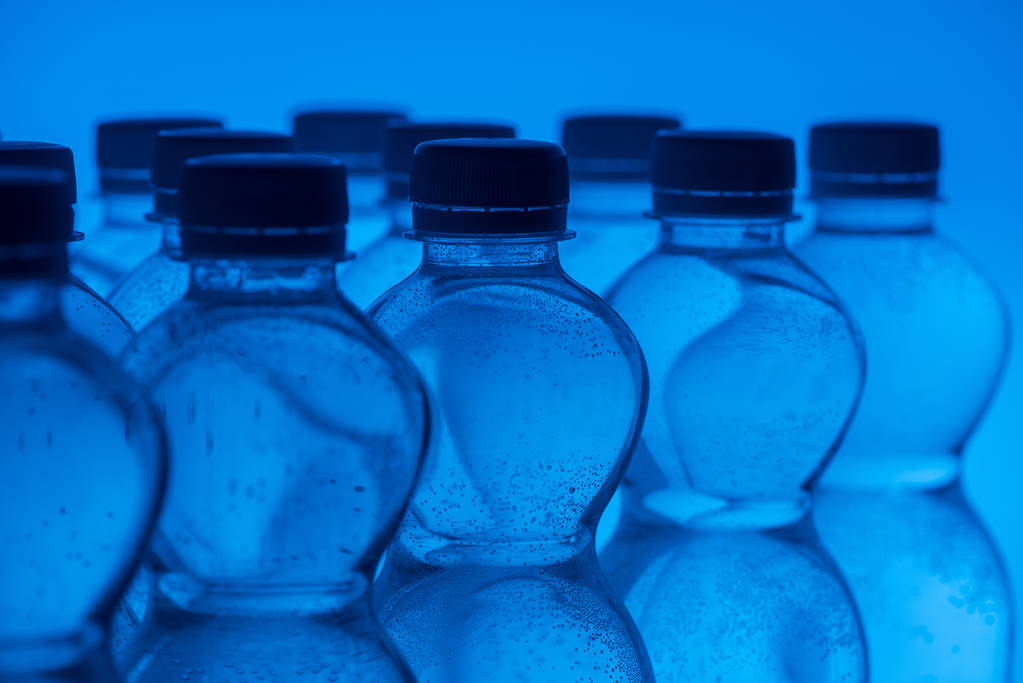 Detail plastových lahví na vodu v řádcích na neon modré pozadí  - Fotografie, Obrázek