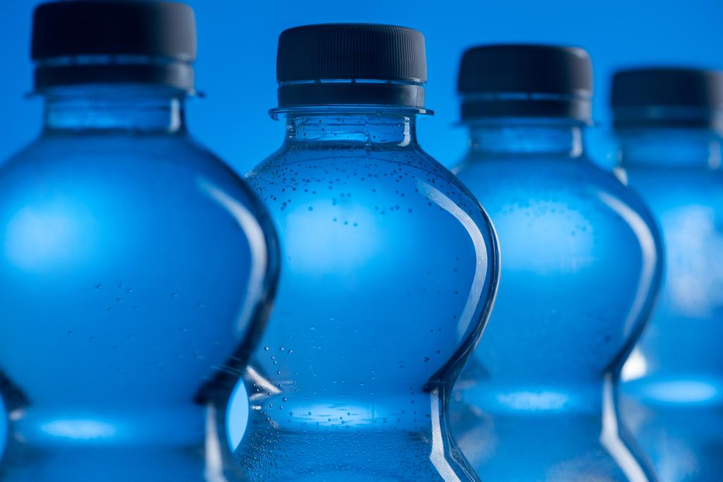 Close up van transparant plastic flessen van water met de bubbels in de rij op blauwe achtergrond - Foto, afbeelding