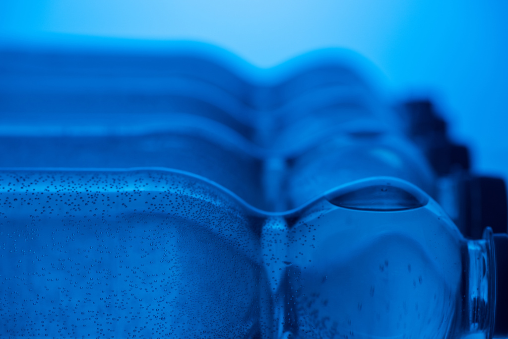 Close up van plastic flessen van water met bubbels en kopieer ruimte op blauwe achtergrond - Foto, afbeelding