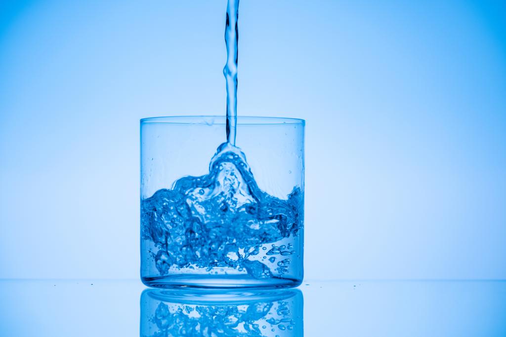 getinte foto van water gieten in glas op blauwe achtergrond - Foto, afbeelding