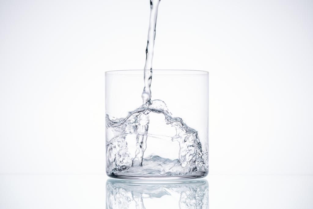 water gieten in glas op witte achtergrond met verlichte en kopie ruimte - Foto, afbeelding