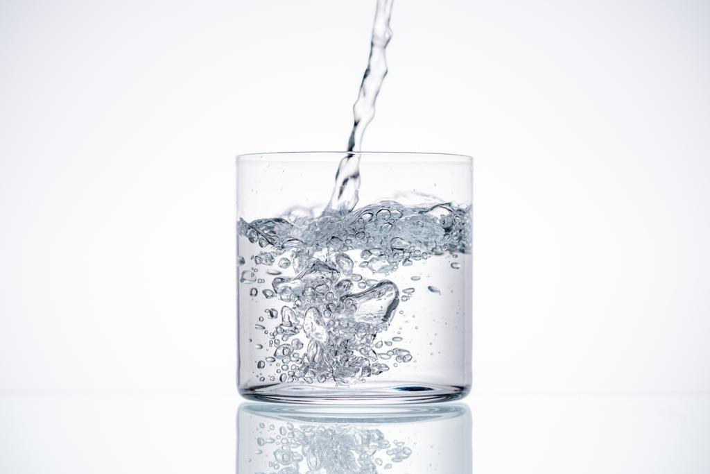 νερό ρίχνει στο πόσιμο γυαλί σε λευκό φόντο με οπίσθιο φωτισμό - Φωτογραφία, εικόνα