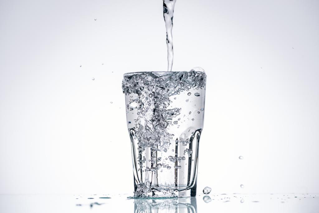 water gieten in vol glas op witte achtergrond met verlichte en spatten - Foto, afbeelding