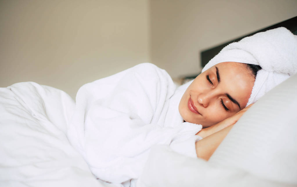 Ομορφιά ύπνου. Κομψό κορίτσι στο ξενοδοχείο άνετος κρεβάτι με μπουρνούζι και μια πετσέτα πάνω της. Κοιμάται μετά από μια δραστήρια μέρα στην παραλία. - Φωτογραφία, εικόνα