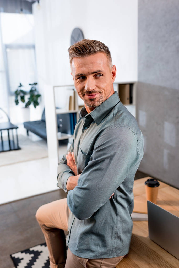 cheerful businessman standing with crossed arms in modern office - Photo, Image