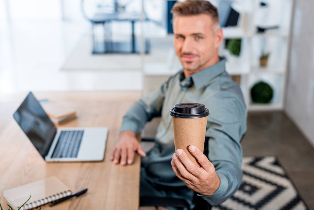 selective focus of paper cup in hand of cheerful businessman in office - Photo, Image