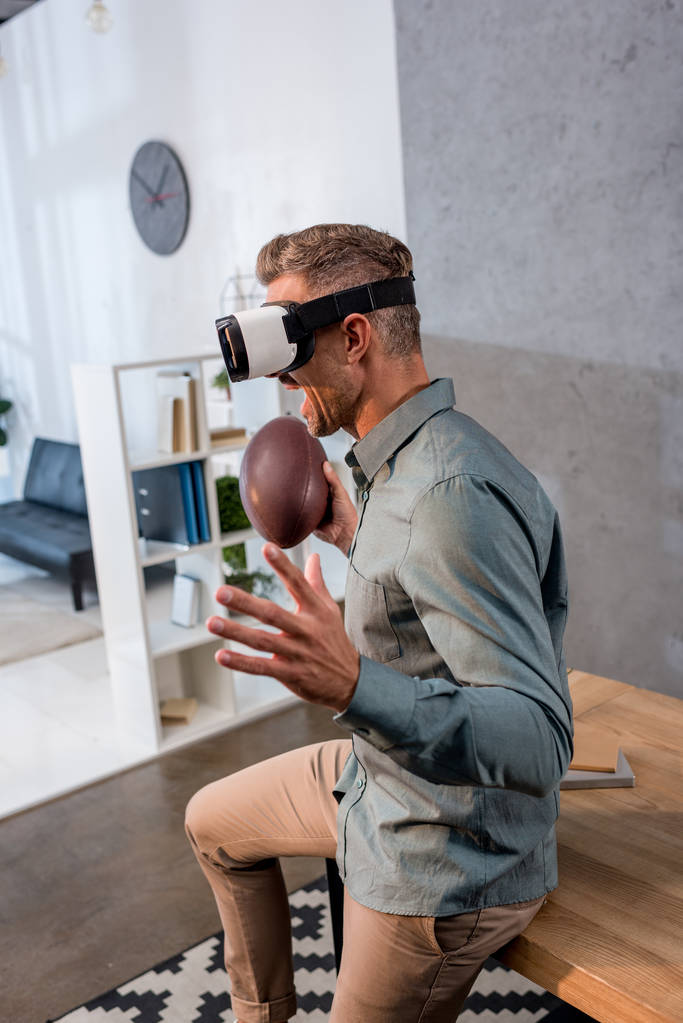 excited businessman wearing virtual reality headset while holding american football  - Photo, Image