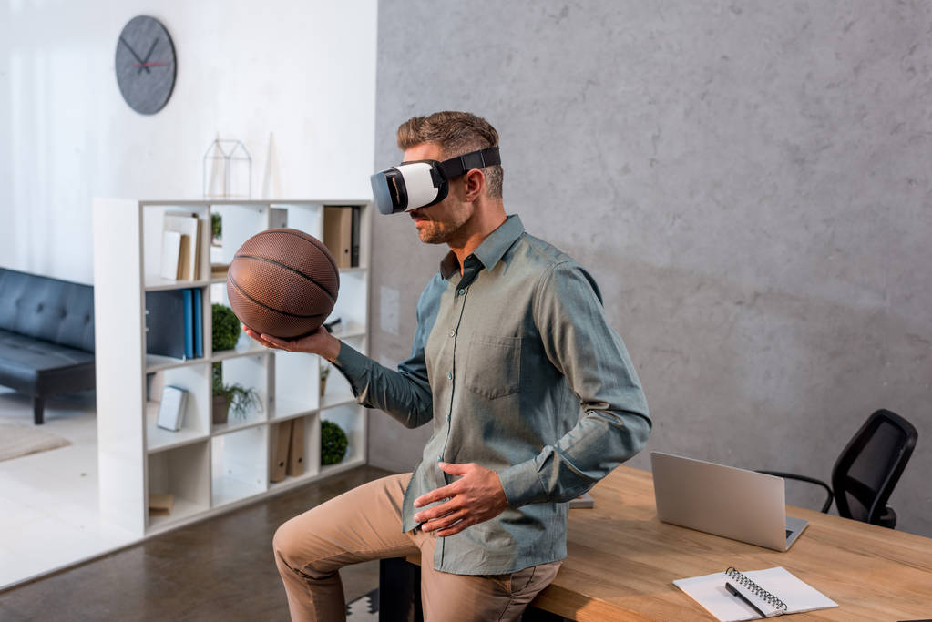 empresário vestindo fone de ouvido realidade virtual e segurando basquete no escritório moderno
 - Foto, Imagem