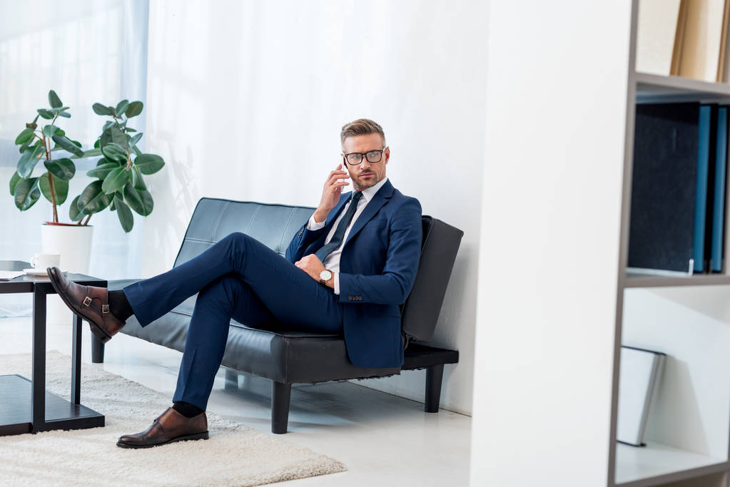 komea liikemies lasit istuu sohvalla ja puhuu älypuhelimella
  - Valokuva, kuva