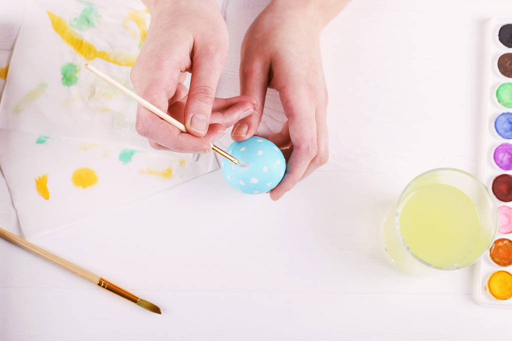 Huevos de Pascua pintados a mano, pinturas y pinceles sobre una mesa blanca. Preparación para las vacaciones. Las manos de las niñas dibujan un patrón
. - Foto, Imagen