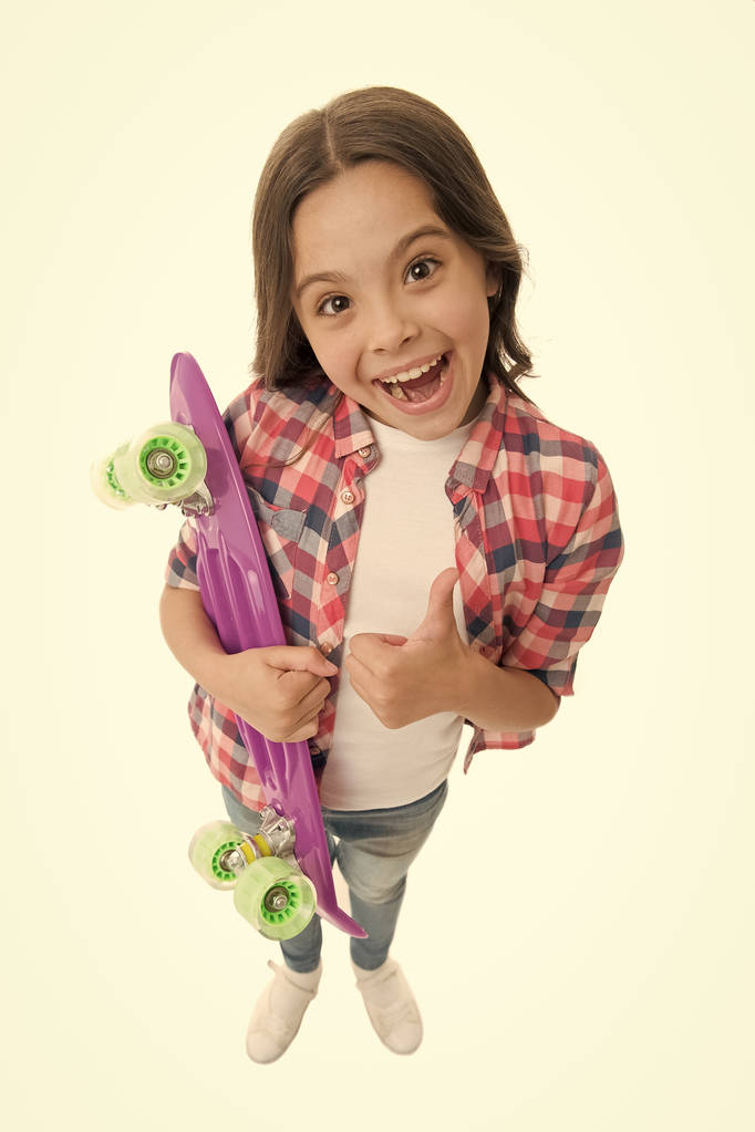 Good choice. Kid girl happy holds penny board. Child likes plastic skateboard shows thumb up. Modern teen hobby. Girl happy face carries penny board white background. Learning how to ride penny board - Photo, Image