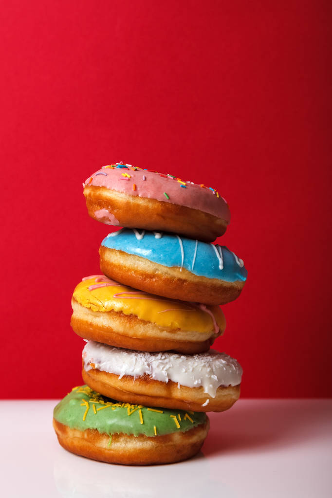 Пончики в різнокольоровій глазурі, укладені один на одного на червоному тлі, копіюють простір. концепція хлібобулочної реклами
 - Фото, зображення