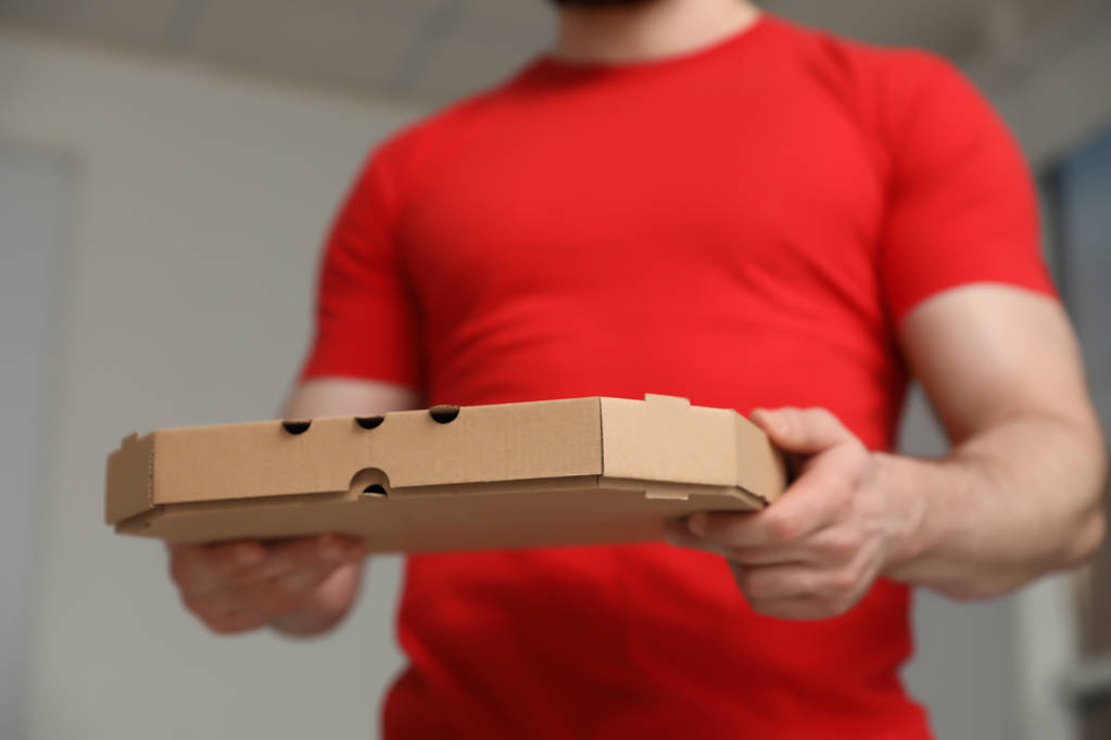 Kuriiri pizzalaatikolla hämärtyneellä taustalla, lähikuva
 - Valokuva, kuva