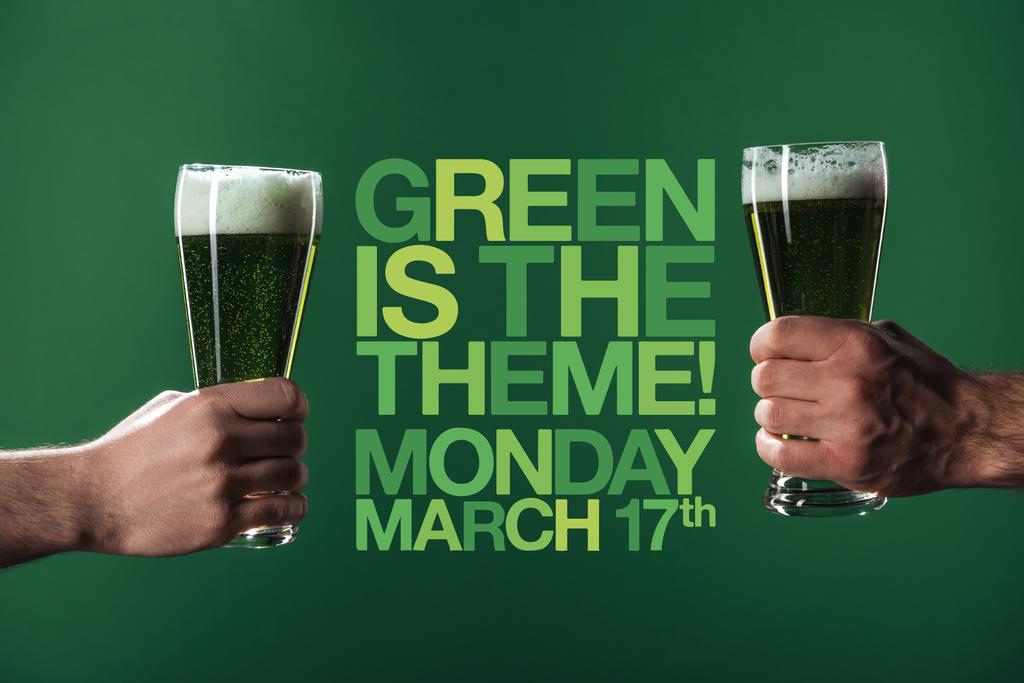 cropped view of men holding glasses of beer with foam near green is the theme lettering on green background - Photo, Image