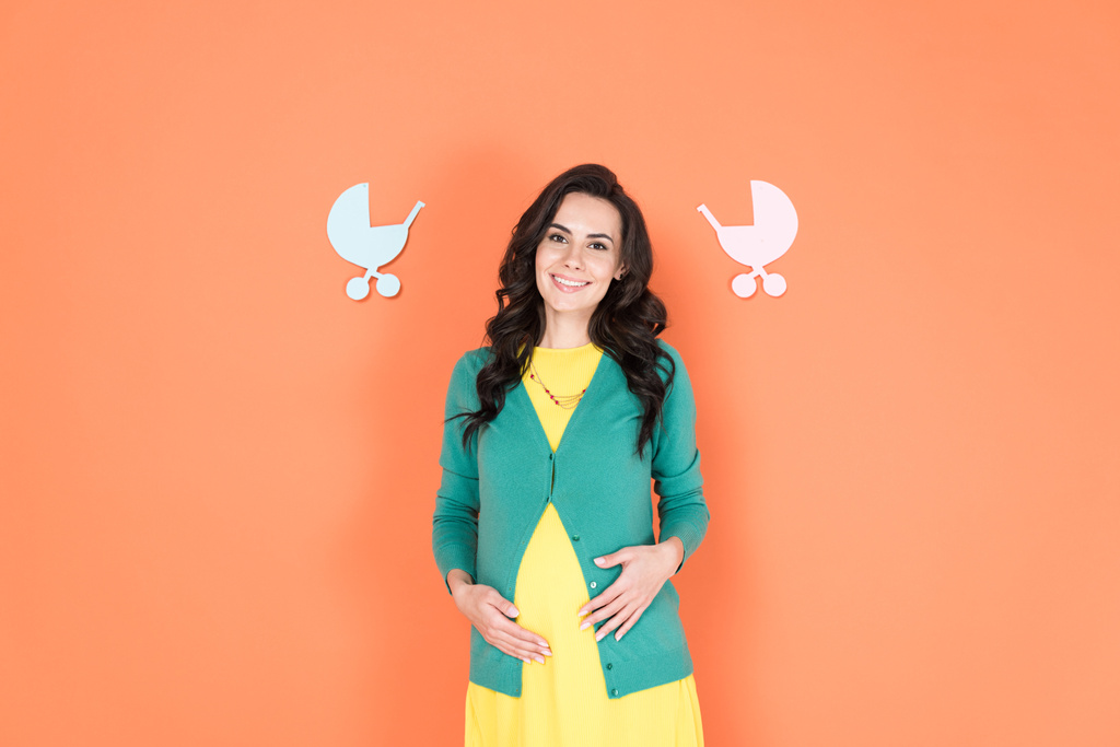 Happy pregnant young woman touching belly on orange background - Photo, Image