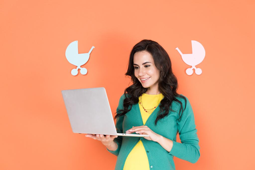 Attractive pregnant woman in green cardigan using laptop on orange background - Photo, Image