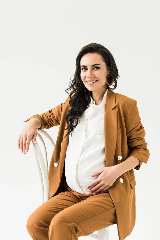 Usměvavá brunetka těhotná žena sedící na židli, izolované na bílém  - Fotografie, Obrázek