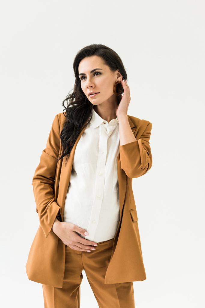 verträumte Schwangere im braunen Anzug berührt Bauch isoliert auf Weiß - Foto, Bild