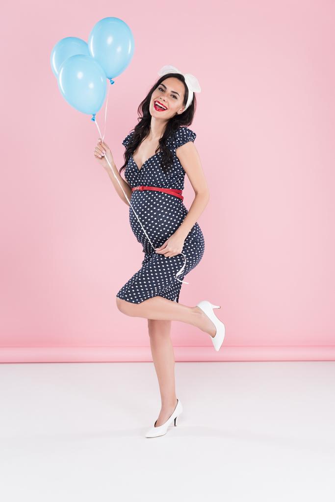 Prachtige zwangere vrouw met lucht ballonnen staande op een been op roze achtergrond - Foto, afbeelding