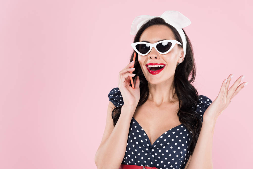 Привлекательная брюнетка в солнцезащитных очках, разговаривающая на смартфоне изолированная на розовом
 - Фото, изображение