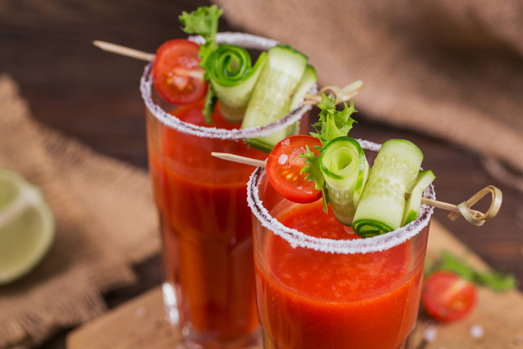 Dwie szklanki soku pomidorowego, ozdobione świeżymi pomidorami, ogórkiem i liści na podłoże drewniane - Zdjęcie, obraz
