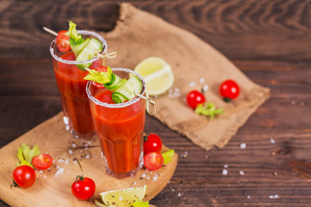 Deux verres de jus de tomate bio frais décorés de tomates crues, de concombre et de feuilles sur une planche à découper rustique en bois
 - Photo, image