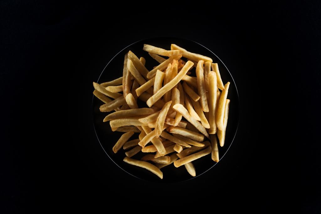 top view of tasty french fries on plate isolated on black - Photo, Image
