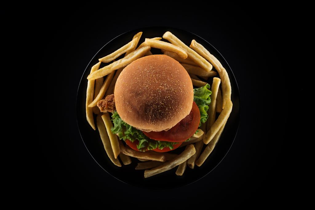vista superior de sabrosas papas fritas y hamburguesa de pollo en el plato aislado en negro
 - Foto, Imagen