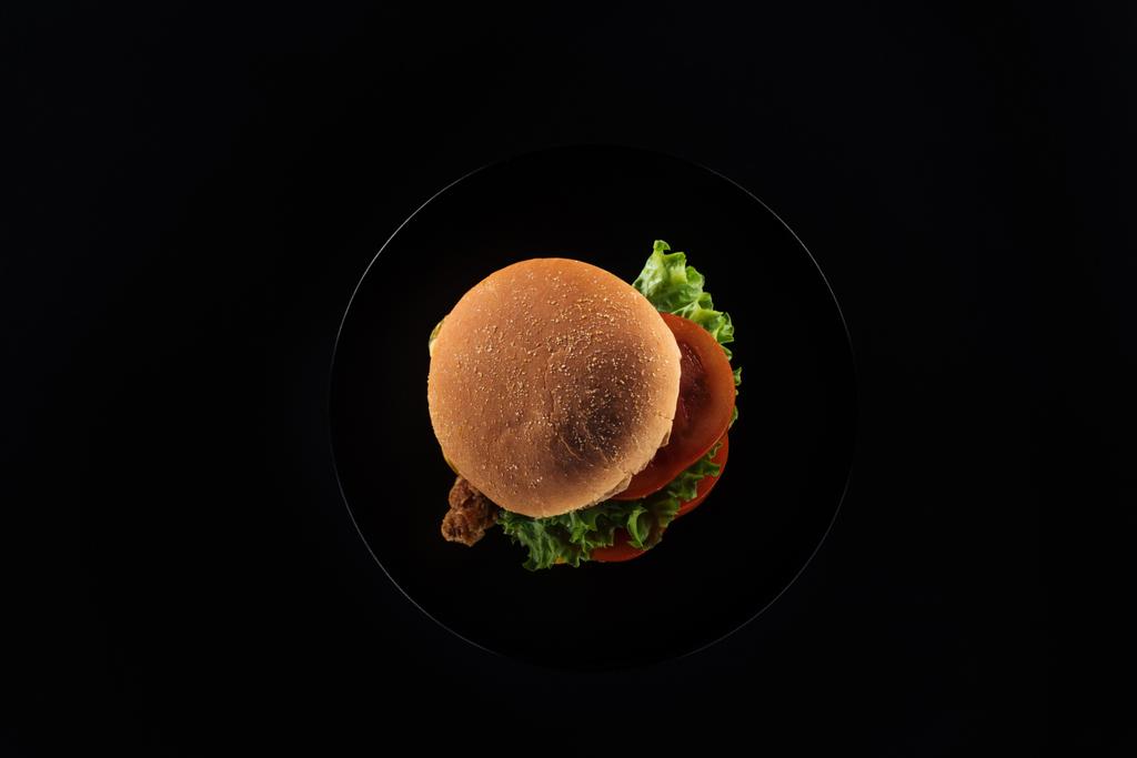 top view of tasty unhealthy chicken burger on plate isolated on black - Photo, Image