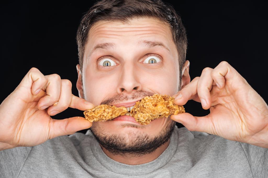 nuggets z kurczaka emocjonalne mężczyzna jedzenie patrząc na kamery na czarnym tle - Zdjęcie, obraz