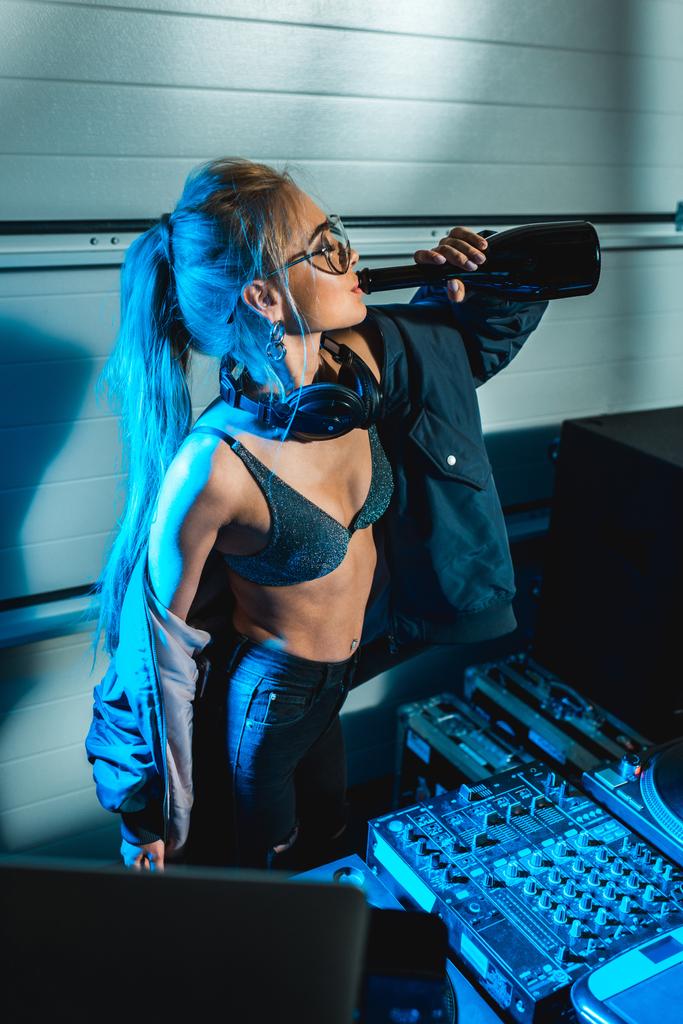 DJ-Frau steht neben DJ-Mixer und trinkt Wein aus Flasche - Foto, Bild