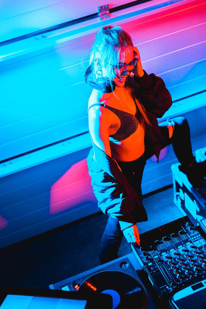 bovenaanzicht van vrolijke dj meisje met blonde haren raken dj mixer in nachtclub - Foto, afbeelding