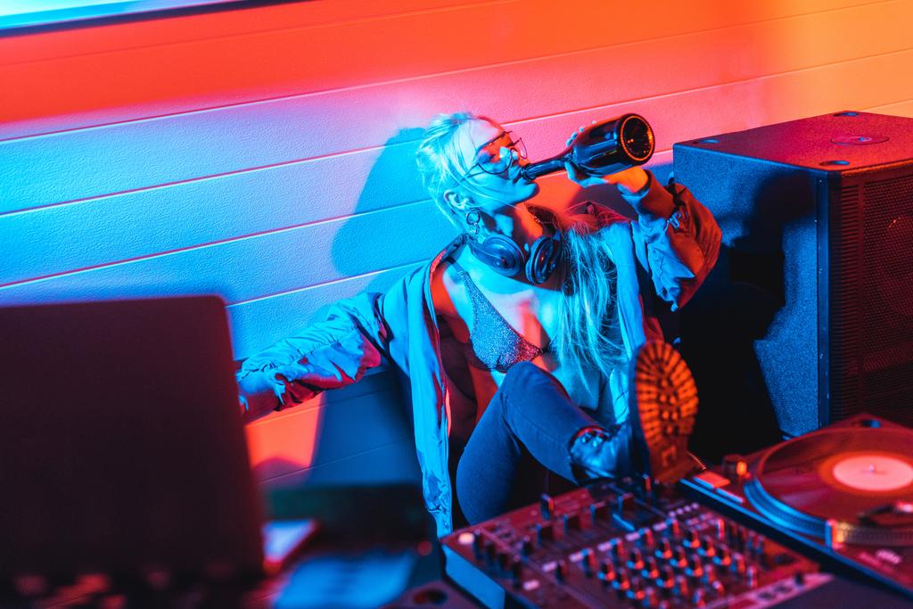 selective focus of attractive dj woman drinking wine from bottle with closed eyes - Photo, Image