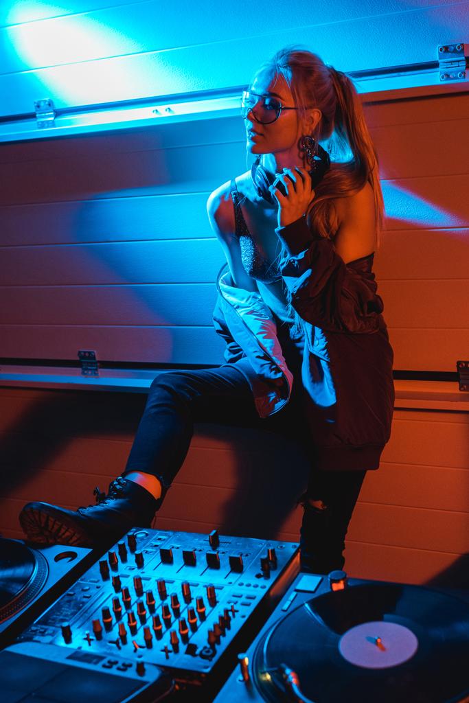atrakcyjny blond dj dziewczyna w okularach stałego i dotykając słuchawki w nocnym klubie - Zdjęcie, obraz